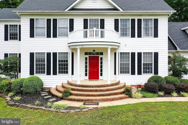 colonial-style house featuring a balcony and a front lawn