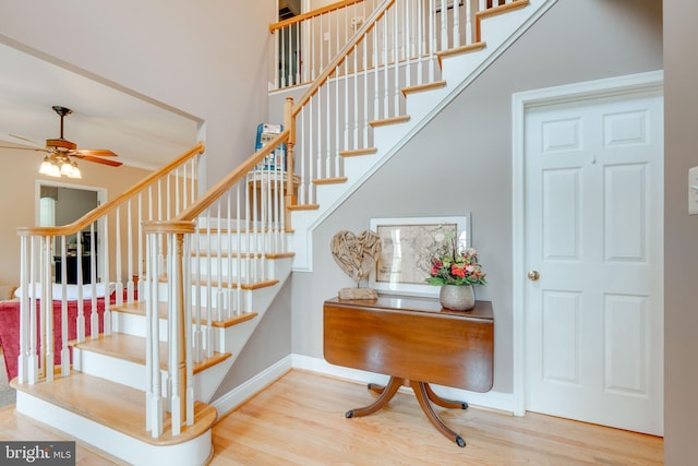 staircase with ceiling fan, a towering ceiling, and hardwood / wood-style floors