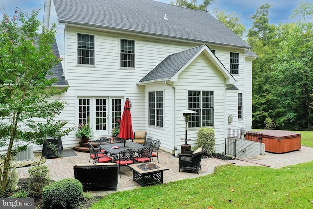 back of house with an outdoor fire pit, a lawn, a patio area, and a hot tub