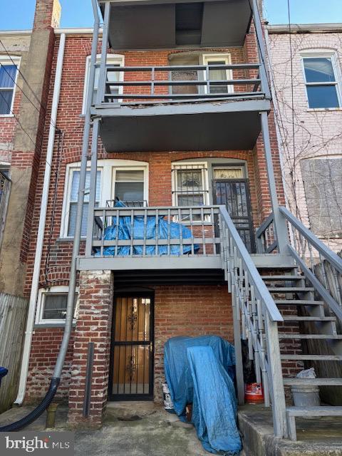 rear view of house featuring brick siding, a balcony, and stairs