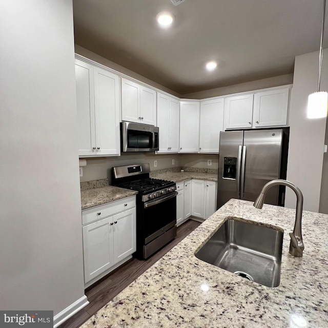 kitchen with light stone counters, white cabinetry, stainless steel appliances, sink, and decorative light fixtures