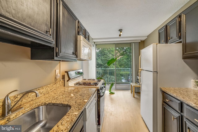 kitchen with light stone counters, light wood-type flooring, white appliances, and sink