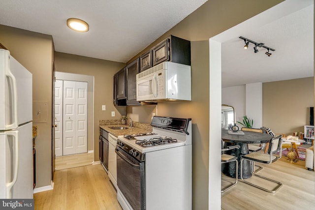 kitchen featuring light wood-type flooring, track lighting, white appliances, dark brown cabinetry, and sink