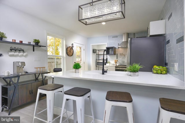 kitchen featuring a kitchen breakfast bar, stainless steel refrigerator, wall chimney exhaust hood, and white cabinets