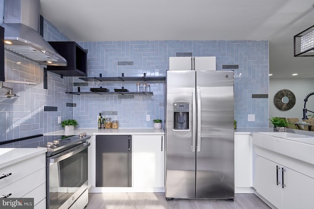 kitchen featuring white cabinets, light hardwood / wood-style flooring, wall chimney range hood, stainless steel appliances, and decorative backsplash