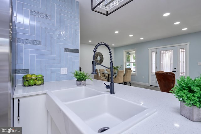 kitchen featuring light stone countertops, white cabinets, stainless steel fridge, and sink