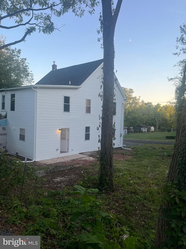 back house at dusk featuring a lawn