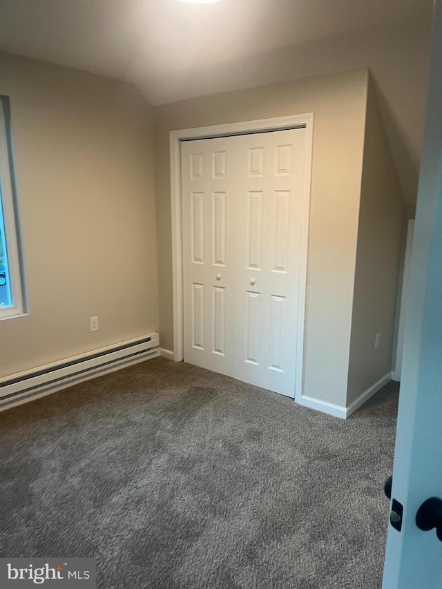 unfurnished bedroom featuring a closet, baseboard heating, and dark colored carpet