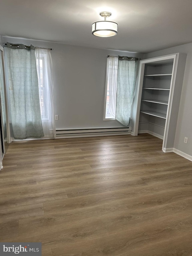 unfurnished bedroom with wood-type flooring and baseboard heating