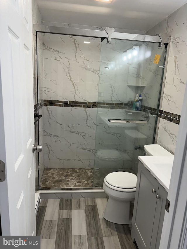 bathroom with tile walls, a shower with door, vanity, and toilet