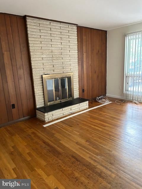 unfurnished living room featuring a fireplace, wood-type flooring, and wooden walls