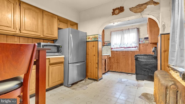 kitchen featuring wooden walls, radiator heating unit, and stainless steel appliances