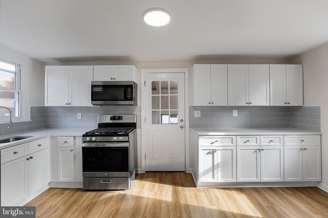 kitchen with white cabinets, stainless steel appliances, tasteful backsplash, and light hardwood / wood-style flooring