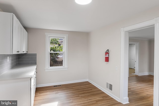 kitchen with light hardwood / wood-style flooring, white cabinets, backsplash, and crown molding