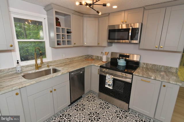 kitchen with sink, a textured ceiling, light stone counters, and stainless steel appliances