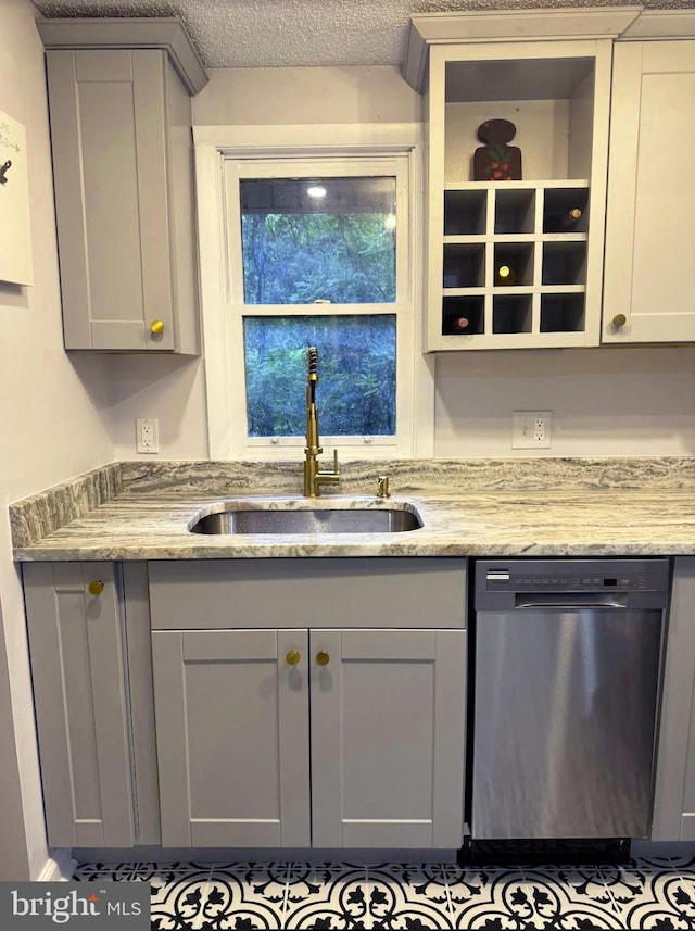 kitchen with gray cabinetry, sink, light stone countertops, stainless steel dishwasher, and a textured ceiling