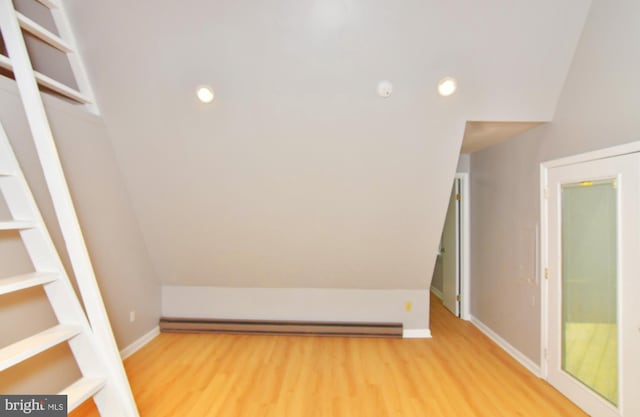 additional living space featuring vaulted ceiling, light hardwood / wood-style flooring, and a baseboard heating unit