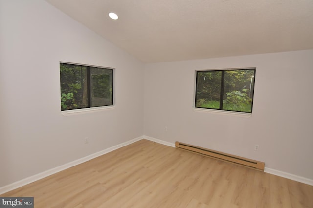 empty room featuring vaulted ceiling, a baseboard heating unit, and light hardwood / wood-style floors