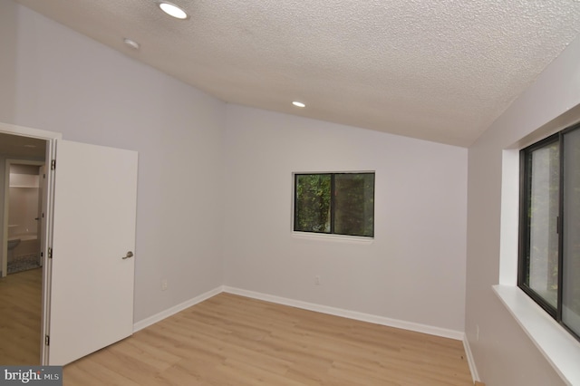 spare room featuring vaulted ceiling, a textured ceiling, and light wood-type flooring