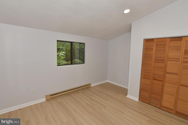 unfurnished bedroom with a closet, a baseboard heating unit, light wood-type flooring, and vaulted ceiling