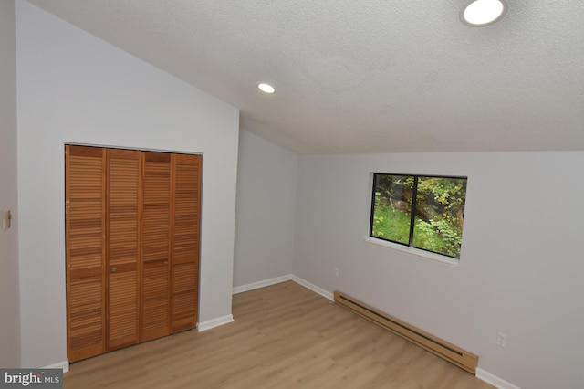 unfurnished bedroom with lofted ceiling, a closet, light wood-type flooring, a baseboard radiator, and a textured ceiling