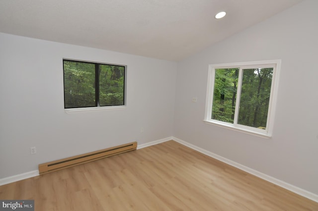 spare room featuring vaulted ceiling, a baseboard radiator, and light wood-type flooring