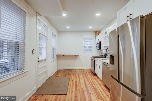 kitchen with appliances with stainless steel finishes, a healthy amount of sunlight, light hardwood / wood-style floors, and white cabinetry