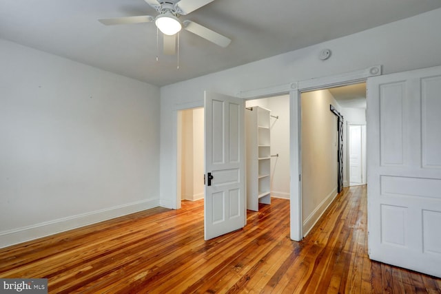 unfurnished bedroom with a spacious closet, ceiling fan, a closet, and hardwood / wood-style flooring