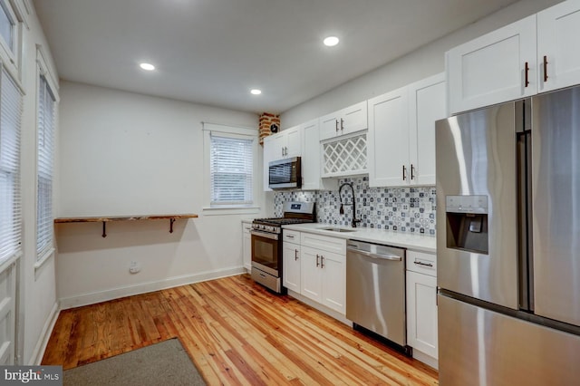 kitchen with white cabinets, sink, light hardwood / wood-style flooring, backsplash, and appliances with stainless steel finishes