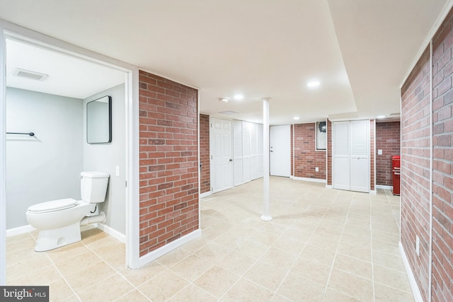 bathroom with tile patterned flooring, brick wall, and toilet