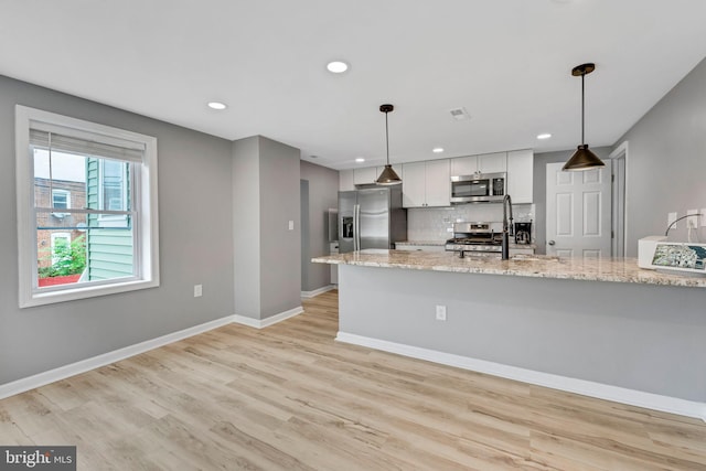 kitchen featuring hanging light fixtures, white cabinetry, stainless steel appliances, and light stone counters