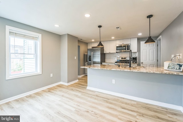 kitchen featuring pendant lighting, stainless steel appliances, white cabinets, and light stone counters