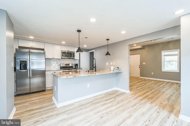 kitchen with appliances with stainless steel finishes, white cabinetry, kitchen peninsula, light stone countertops, and sink