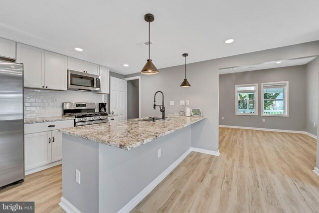 kitchen featuring stainless steel appliances, white cabinets, light stone counters, and decorative light fixtures