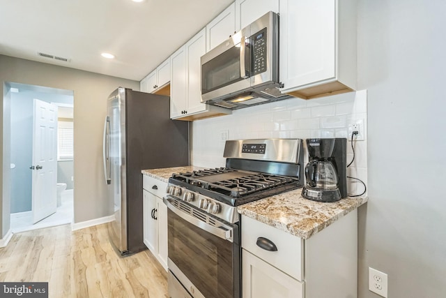 kitchen featuring appliances with stainless steel finishes, white cabinetry, backsplash, light stone countertops, and light hardwood / wood-style flooring