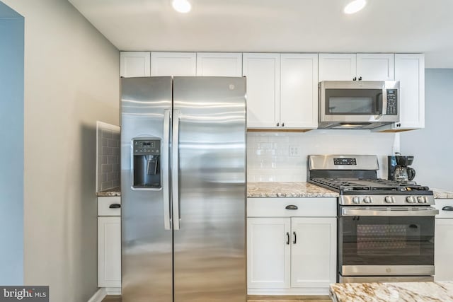 kitchen featuring light stone countertops, stainless steel appliances, white cabinetry, and backsplash