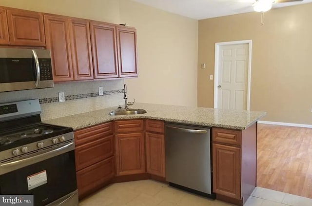 kitchen featuring light stone counters, sink, kitchen peninsula, backsplash, and appliances with stainless steel finishes