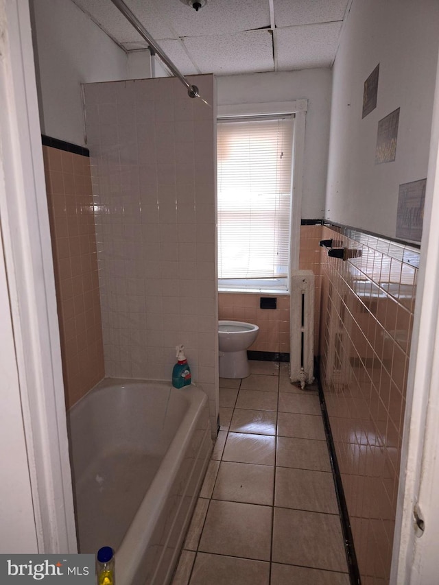 bathroom with radiator, toilet, tiled shower / bath combo, tile walls, and tile patterned flooring