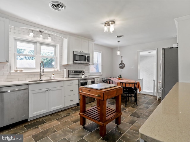 kitchen with appliances with stainless steel finishes, white cabinetry, sink, and decorative light fixtures