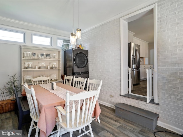 dining space featuring dark hardwood / wood-style floors, crown molding, stacked washer and clothes dryer, and brick wall