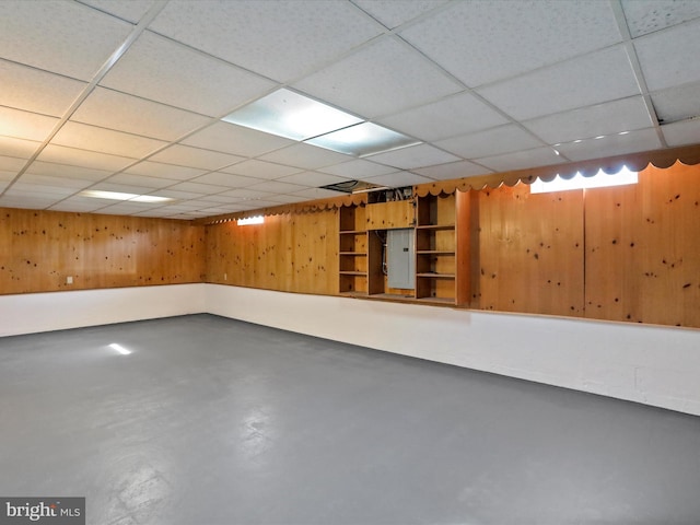 basement featuring wooden walls and a paneled ceiling