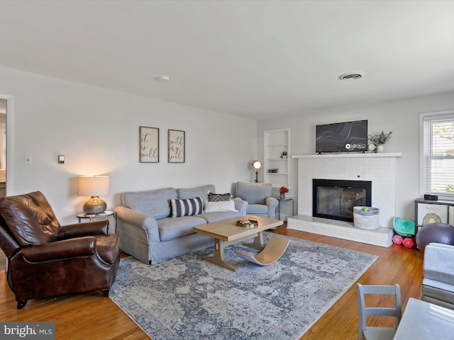 living room featuring a brick fireplace, hardwood / wood-style floors, and built in features