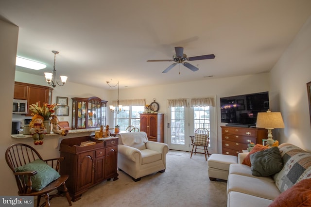 carpeted living room featuring ceiling fan with notable chandelier