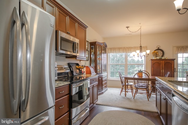 kitchen with pendant lighting, dark wood-type flooring, a notable chandelier, appliances with stainless steel finishes, and light stone countertops