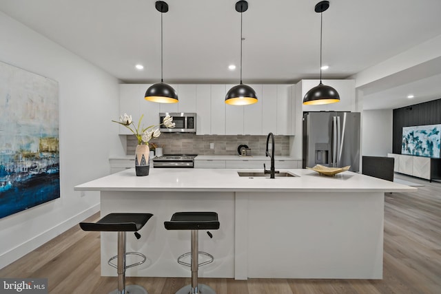 kitchen with pendant lighting, light hardwood / wood-style floors, sink, backsplash, and appliances with stainless steel finishes