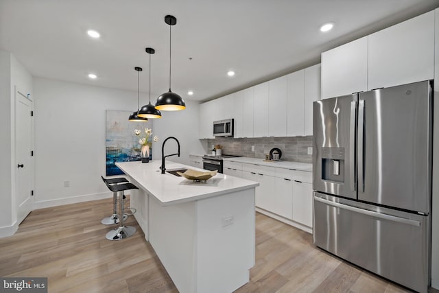 kitchen featuring hanging light fixtures, a center island with sink, white cabinetry, stainless steel appliances, and light hardwood / wood-style floors