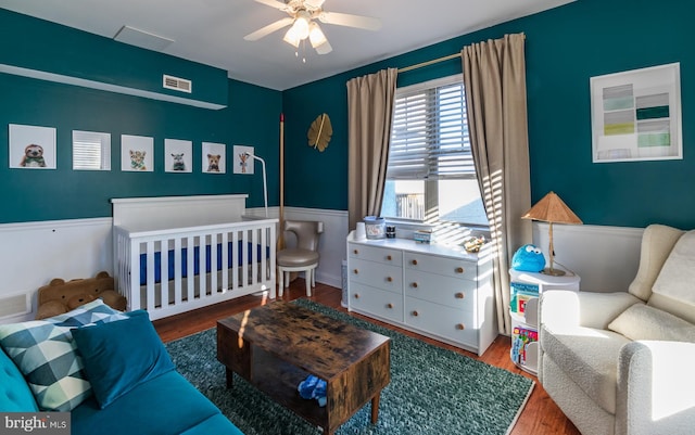 bedroom featuring ceiling fan, a nursery area, and hardwood / wood-style floors