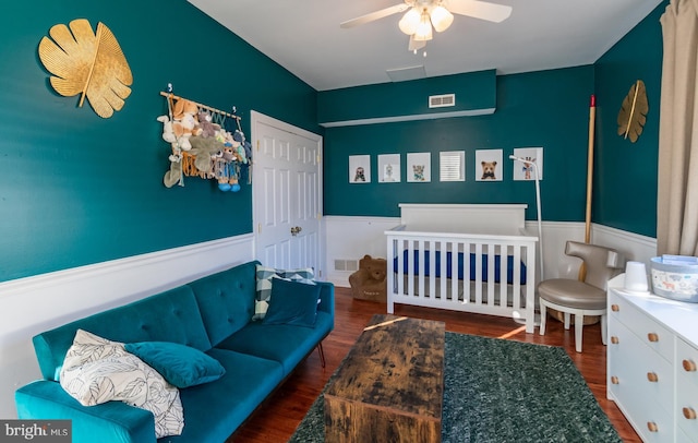 bedroom with ceiling fan, a crib, and dark hardwood / wood-style flooring