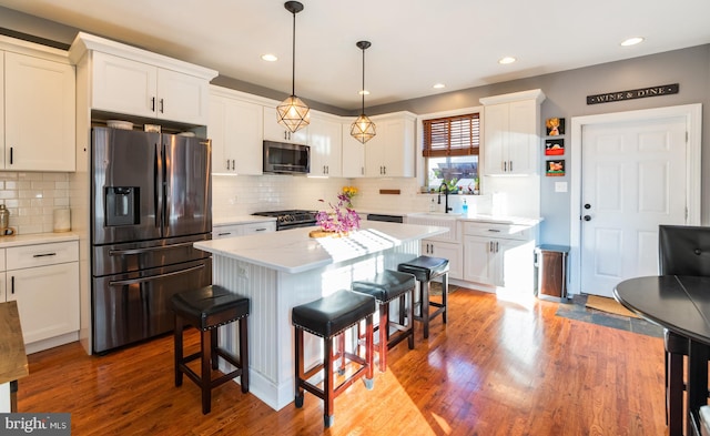 kitchen featuring hanging light fixtures, white cabinetry, stainless steel appliances, a center island, and hardwood / wood-style floors