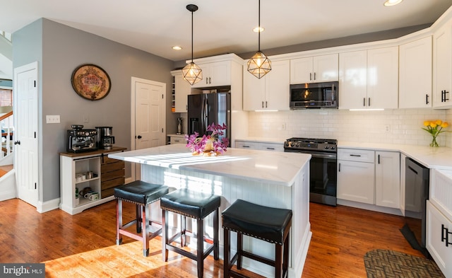 kitchen with stainless steel appliances, white cabinetry, a kitchen island, and hardwood / wood-style floors